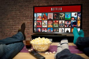 Personas recostadas frente a la TV viendo Netflix y comiendo palomitas de maíz